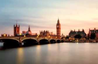 Big Ben and the Houses of Parliament illuminated at dusk across the River Thames with Westminster Bridge in the foreground.
