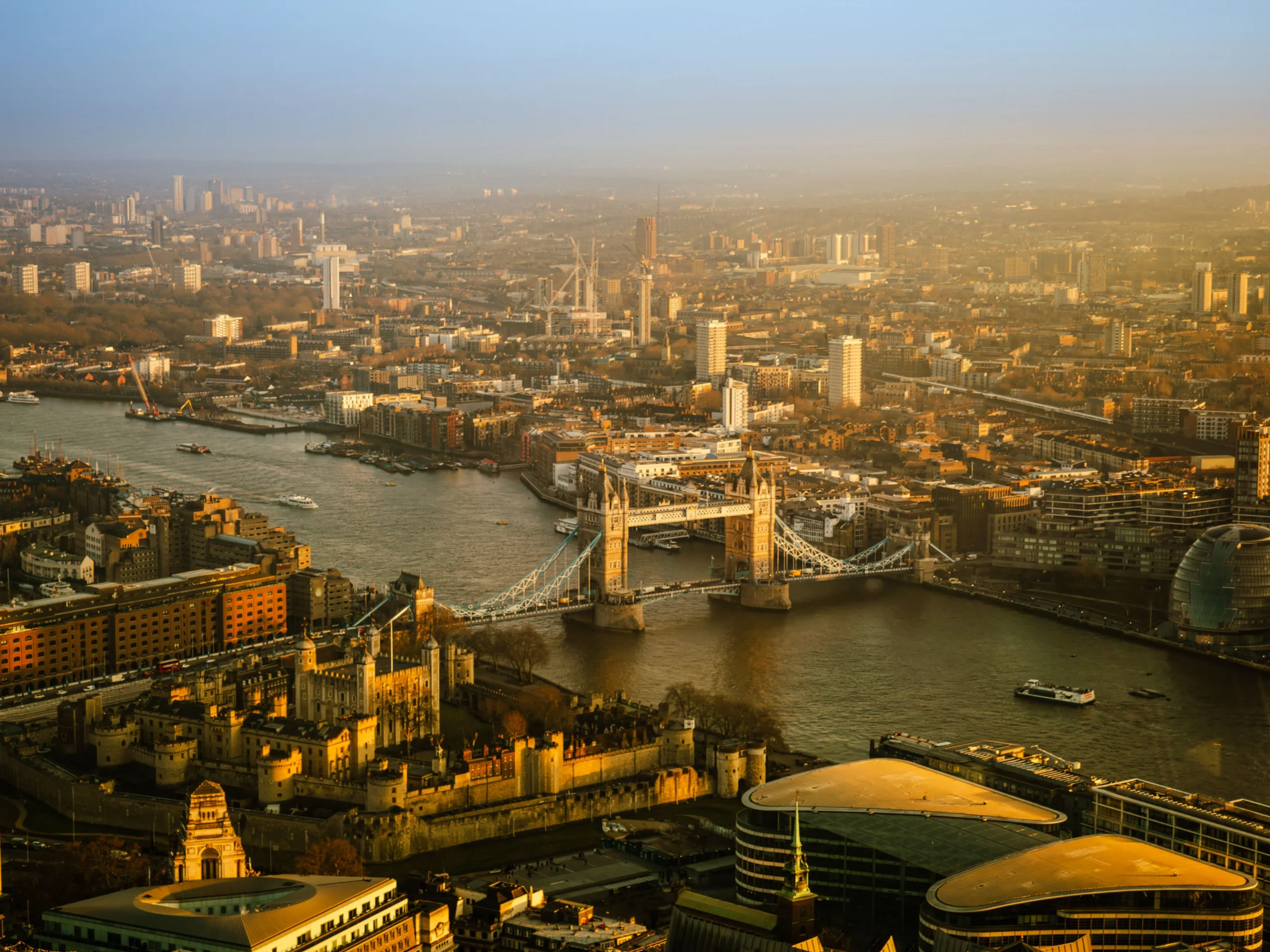 Tower Bridge over the River Thames at golden hour with City of London skyline behind.