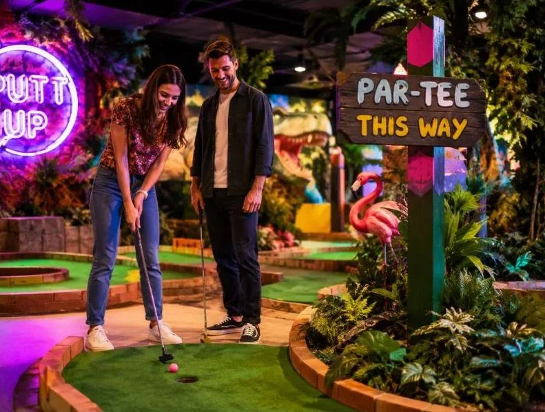 Colourful crazy-golf course interior with a couple mid-swing
