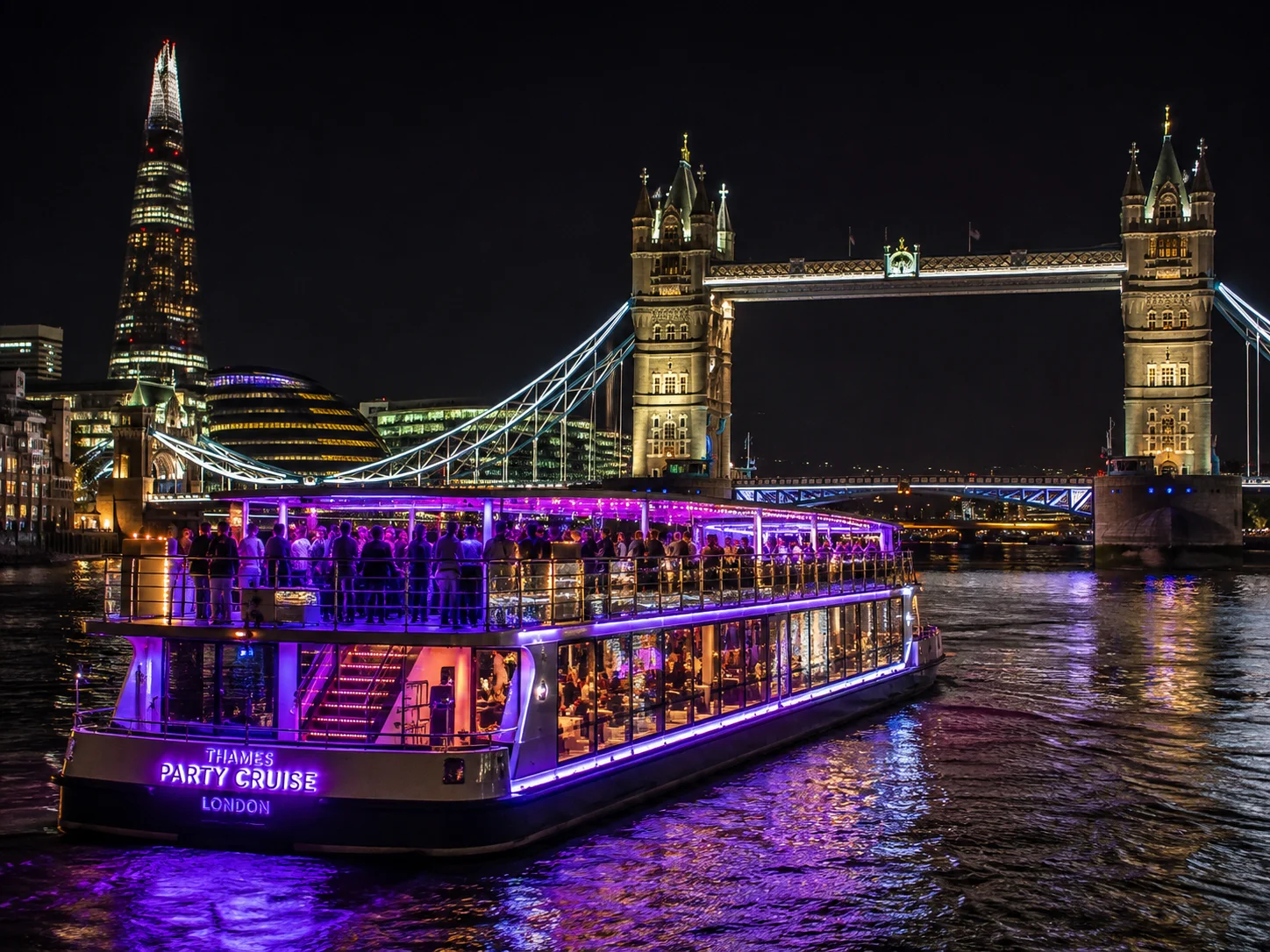 A party boat on the Thames lit up at night by Tower Bridge