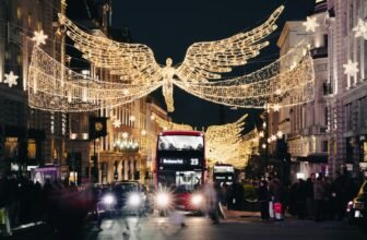 A London street at night lined with large illuminated angel decorations suspended above the road, with buses and shoppers below