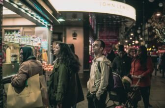 Shoppers queuing in a line along the pavement beside a brightly lit London store after dark